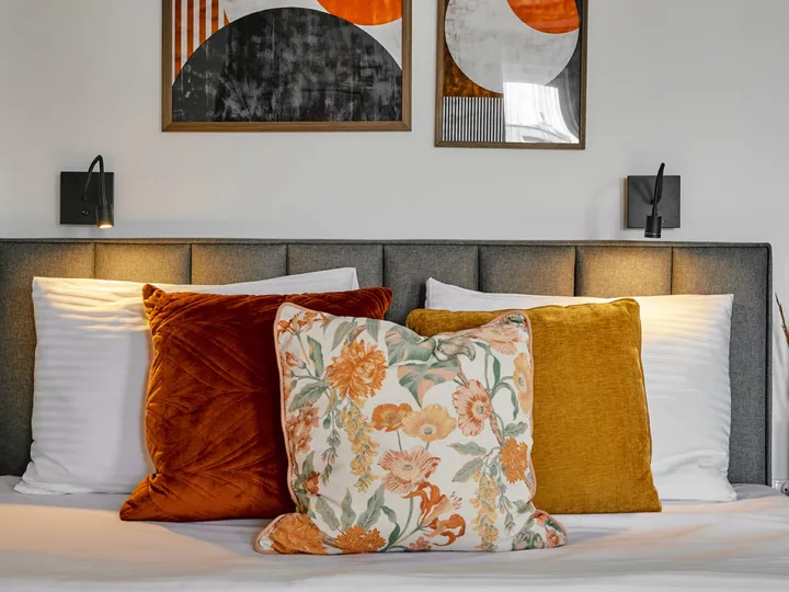 Bed with orange cushions and prints above the headboard