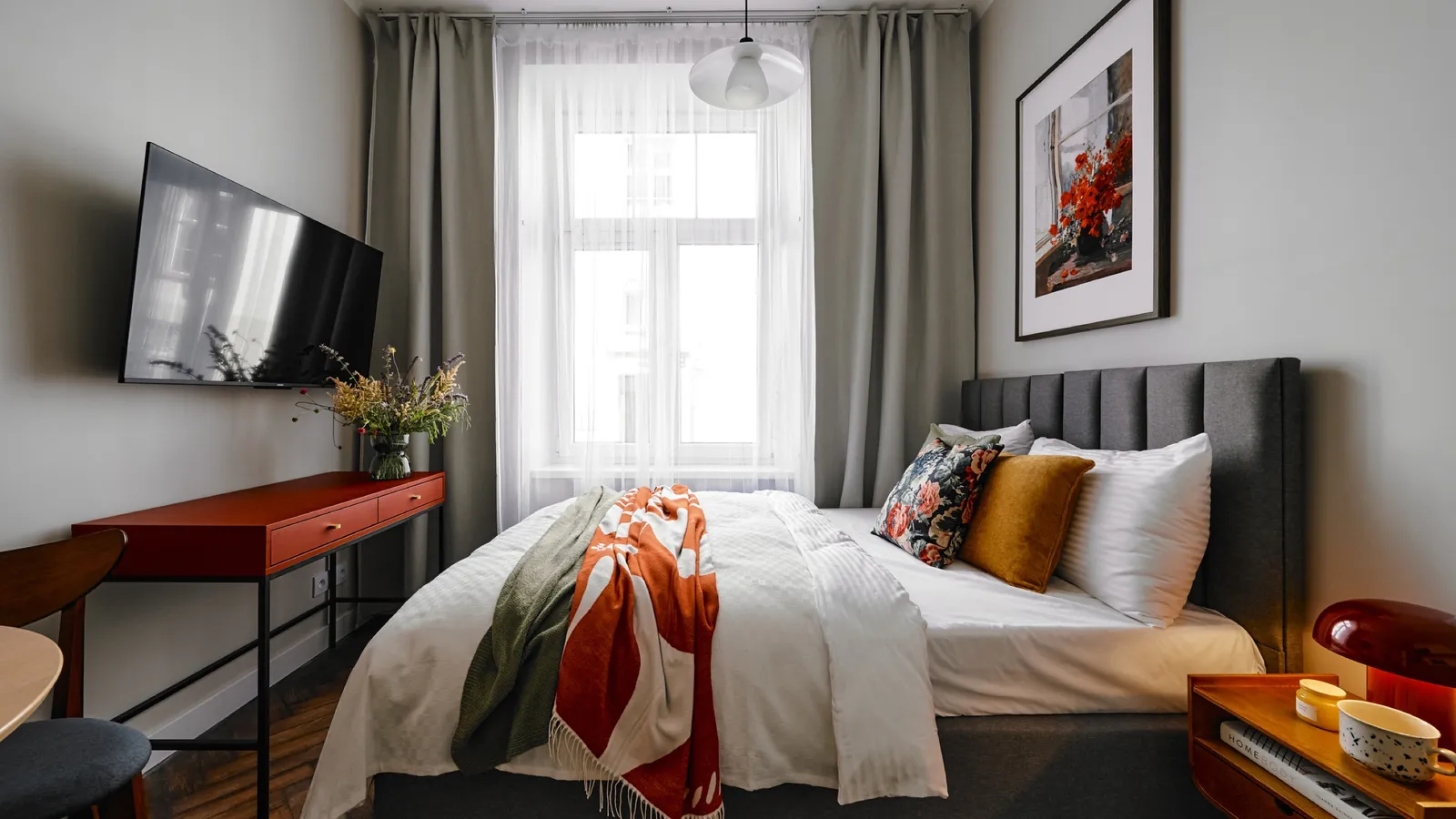 Studio with the bed, a red desk and a curtained window