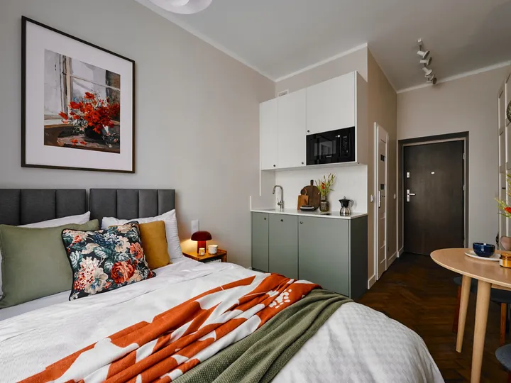 Bed with a colourful throw and the kitchenette behind